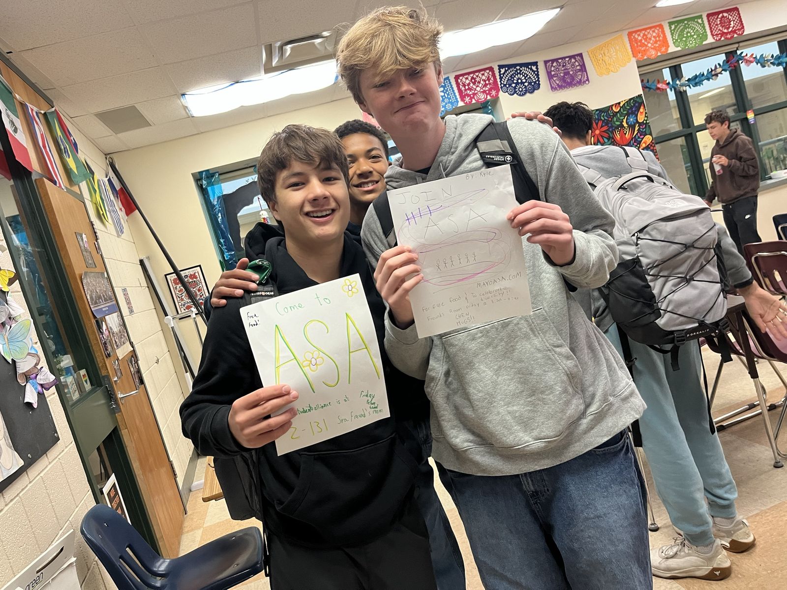 Three friends holding up hand-drawn ASA posters