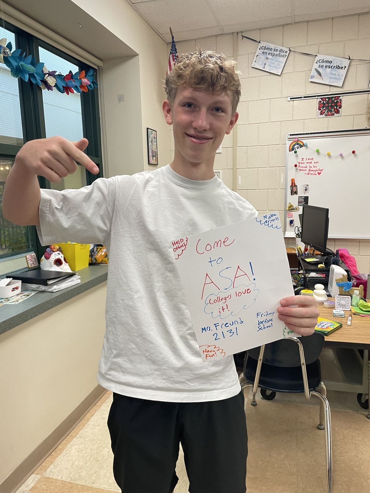 A student pointing at his "Come to ASA! Colleges love it!" poster